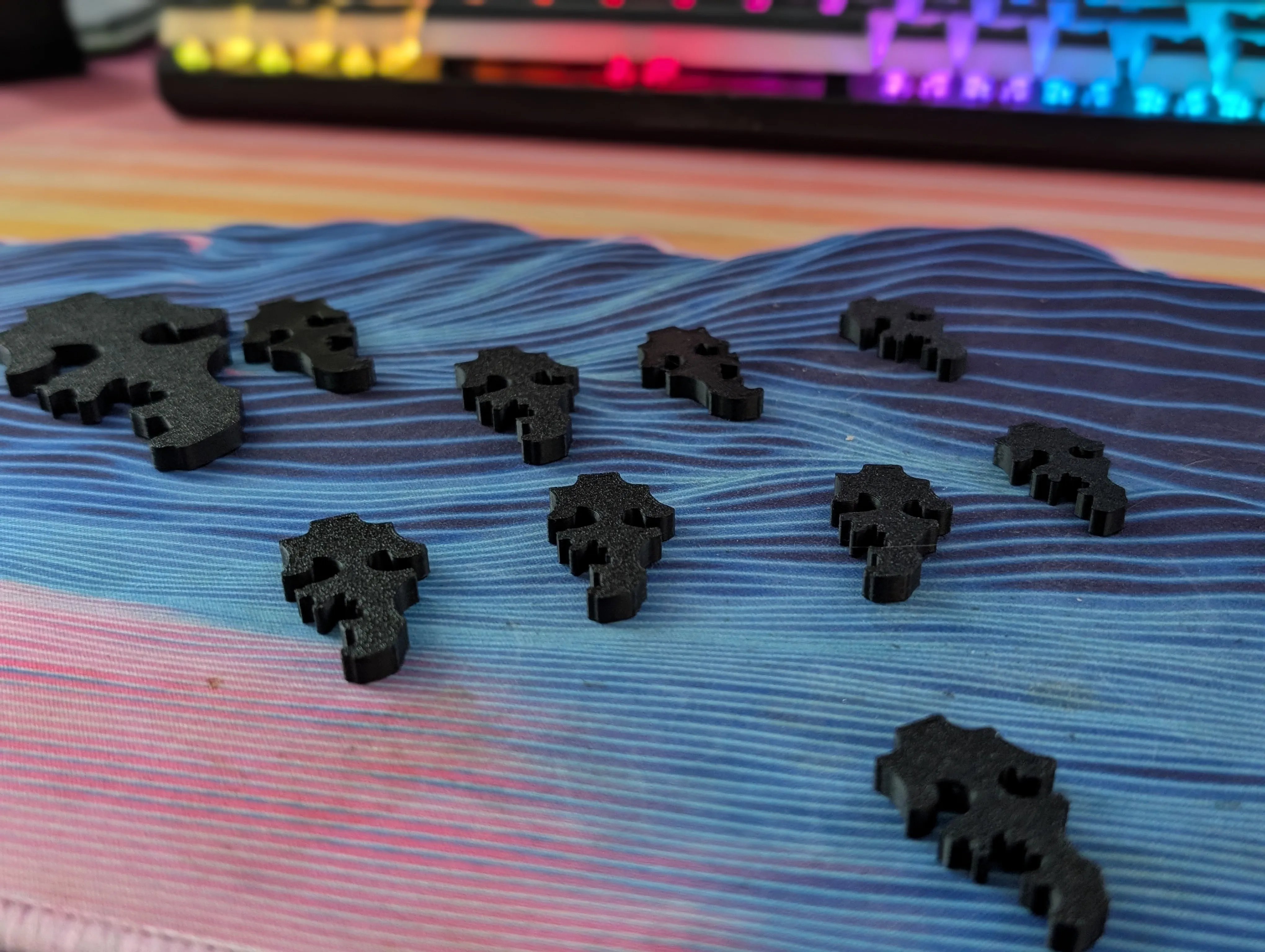 A row of black 3d printed puzzle pieces in progressively smaller sizes sitting on a desk mat in front of a keyboard